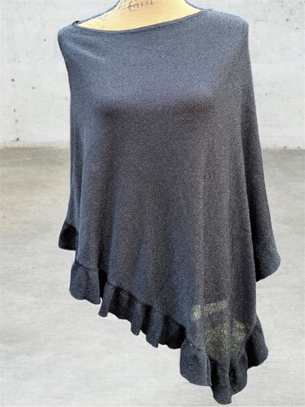 black asymmetrical poncho features a delicate ruffle along the hem. Black silver